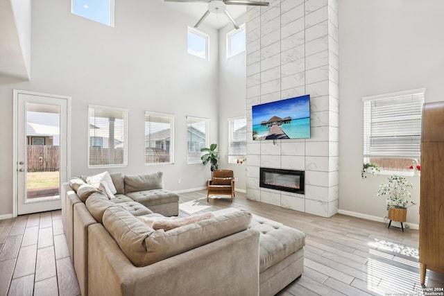 living room featuring a tiled fireplace, ceiling fan, a towering ceiling, and light wood-type flooring