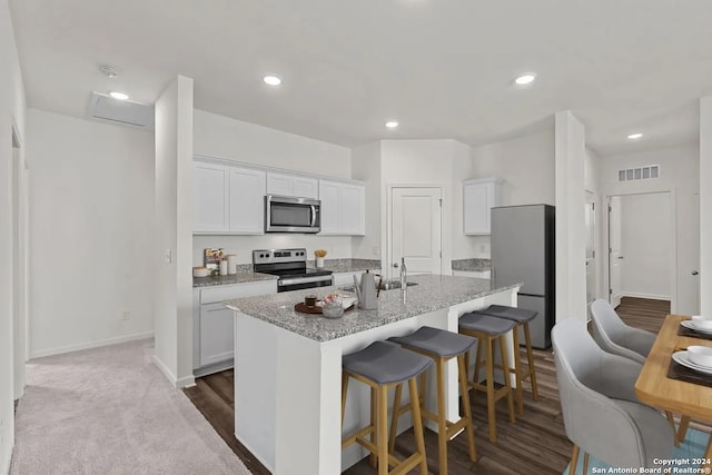 kitchen featuring white cabinets, light stone countertops, an island with sink, and appliances with stainless steel finishes