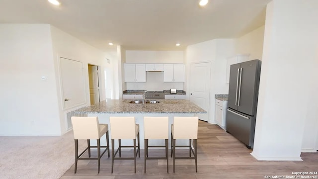 kitchen with stainless steel fridge, light stone counters, a center island with sink, light hardwood / wood-style flooring, and white cabinets