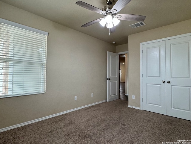 unfurnished bedroom with dark colored carpet, a closet, and ceiling fan