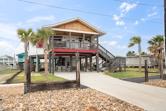 raised beach house featuring covered porch, ceiling fan, a carport, and a front yard