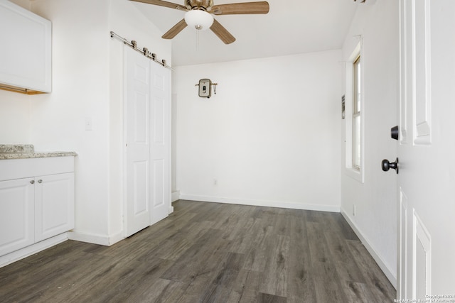 unfurnished room with a barn door, ceiling fan, and dark hardwood / wood-style floors