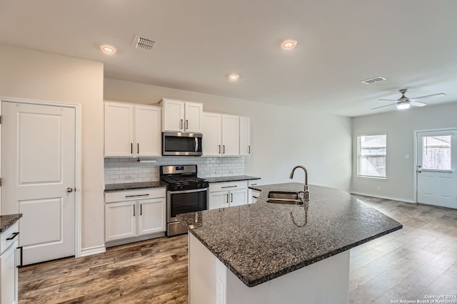 kitchen with white cabinets, sink, hardwood / wood-style floors, appliances with stainless steel finishes, and a kitchen island with sink