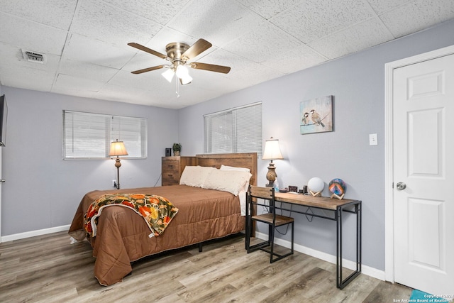 bedroom with wood-type flooring, a drop ceiling, and ceiling fan