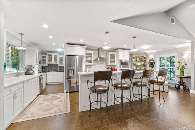 kitchen with white cabinetry, hanging light fixtures, stainless steel appliances, wall chimney range hood, and a kitchen island