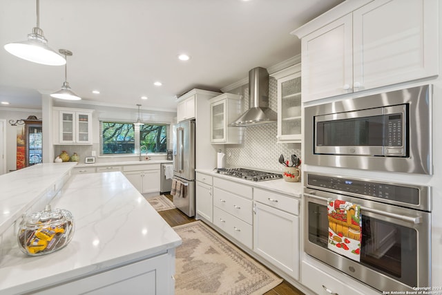 kitchen with appliances with stainless steel finishes, backsplash, ornamental molding, wall chimney exhaust hood, and white cabinets