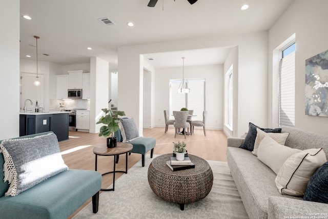 living room with ceiling fan, sink, and light wood-type flooring