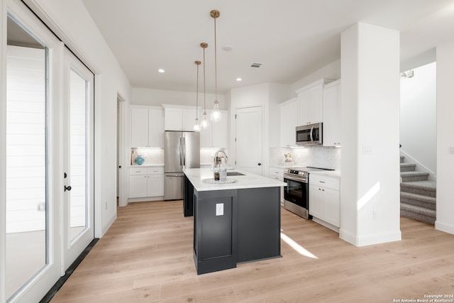 kitchen featuring white cabinetry, pendant lighting, a kitchen island with sink, light hardwood / wood-style floors, and stainless steel appliances