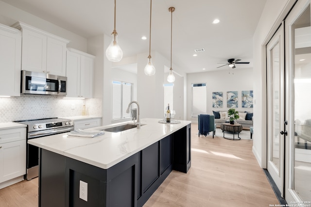 kitchen featuring stainless steel appliances, sink, decorative light fixtures, a center island with sink, and white cabinetry