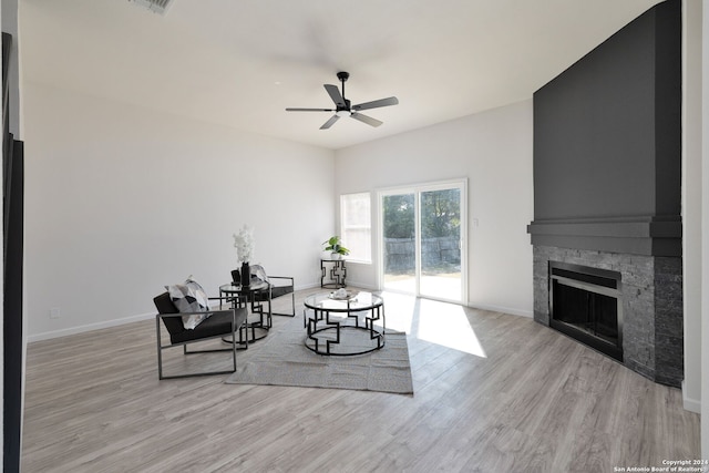 living room with light hardwood / wood-style floors, a stone fireplace, and ceiling fan