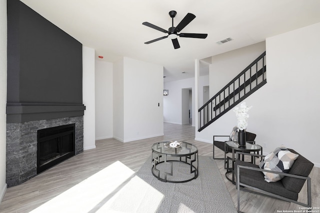 living room featuring a stone fireplace, ceiling fan, and light hardwood / wood-style floors