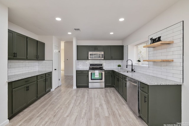 kitchen featuring sink, decorative backsplash, appliances with stainless steel finishes, light wood-type flooring, and light stone counters