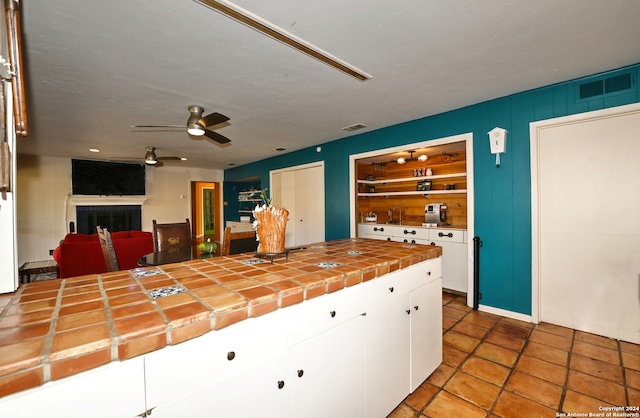 kitchen with built in shelves, white cabinetry, ceiling fan, tile patterned floors, and tile countertops