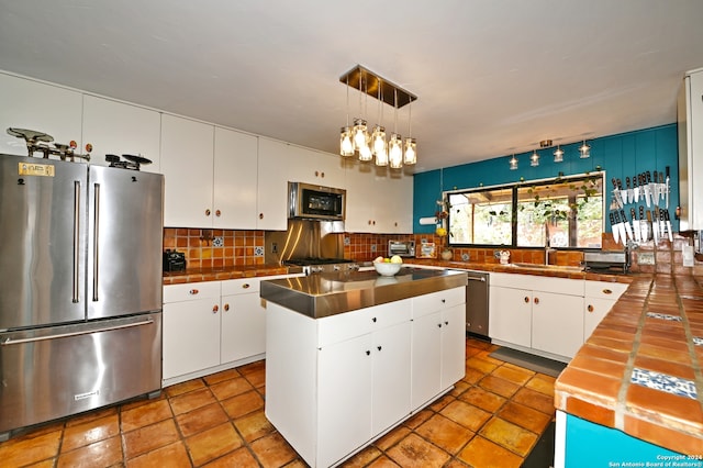 kitchen with appliances with stainless steel finishes, backsplash, pendant lighting, white cabinets, and a center island