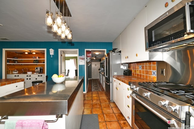 kitchen featuring stainless steel appliances, light tile patterned floors, tasteful backsplash, pendant lighting, and white cabinets