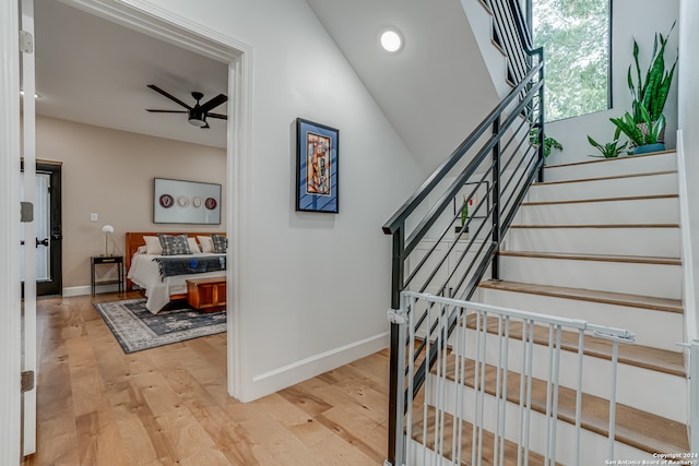 stairs with ceiling fan, wood-type flooring, and vaulted ceiling