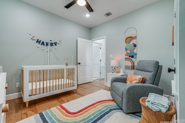 bedroom featuring a crib, ceiling fan, and light hardwood / wood-style floors