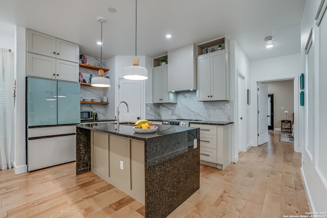 kitchen with sink, light hardwood / wood-style flooring, backsplash, dark stone countertops, and an island with sink