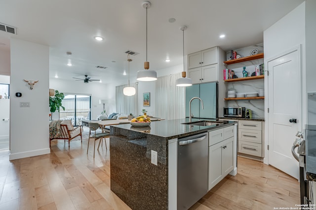 kitchen featuring appliances with stainless steel finishes, dark stone counters, a center island with sink, light hardwood / wood-style floors, and white cabinetry