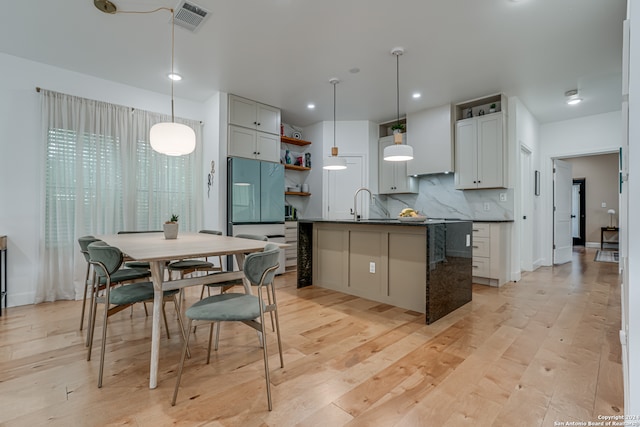 kitchen with white cabinetry, tasteful backsplash, pendant lighting, light hardwood / wood-style floors, and a kitchen island with sink