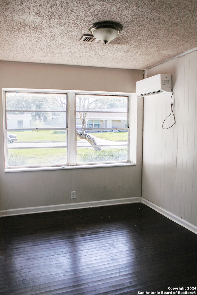 unfurnished room featuring dark hardwood / wood-style flooring, wooden walls, a wall mounted AC, and a healthy amount of sunlight