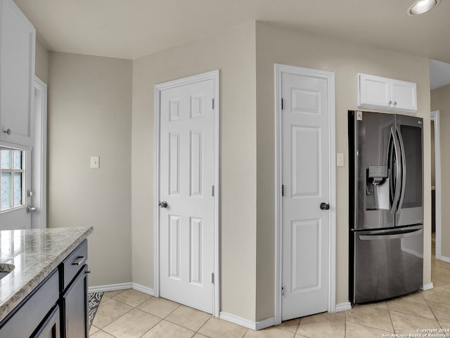 kitchen featuring light stone countertops, stainless steel fridge with ice dispenser, light tile patterned floors, and white cabinetry