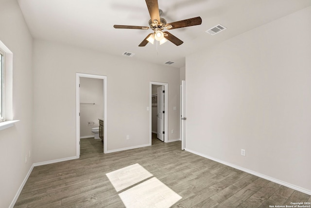 unfurnished bedroom featuring ensuite bathroom, light hardwood / wood-style floors, a walk in closet, and ceiling fan