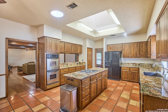 kitchen featuring appliances with stainless steel finishes, a textured ceiling, ceiling fan, sink, and a center island