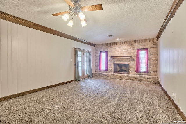 unfurnished living room with carpet, a brick fireplace, a textured ceiling, ceiling fan, and crown molding