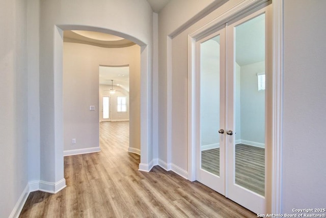 hall featuring french doors, wood finished floors, arched walkways, and baseboards