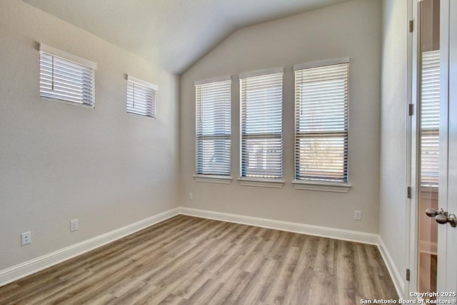 empty room featuring wood finished floors, lofted ceiling, and baseboards