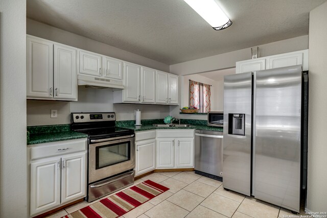 kitchen with appliances with stainless steel finishes, a textured ceiling, sink, white cabinetry, and light tile patterned flooring