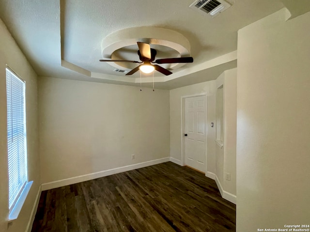 unfurnished room with a raised ceiling, ceiling fan, and dark hardwood / wood-style floors