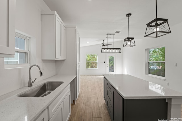 kitchen featuring white cabinets, light stone counters, lofted ceiling, and sink