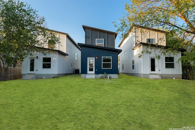 rear view of property featuring a lawn and cooling unit