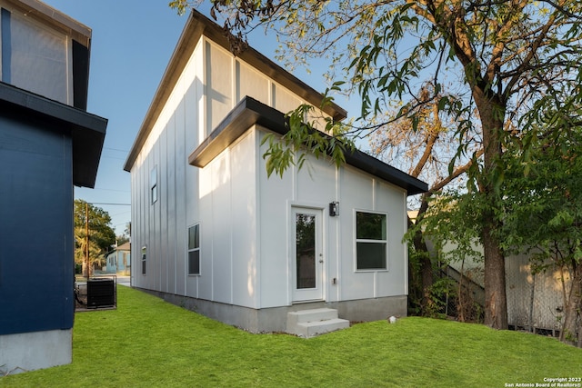 rear view of property featuring central AC unit and a lawn