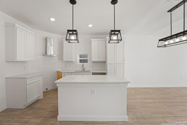 kitchen featuring sink, wall chimney exhaust hood, a kitchen island, pendant lighting, and white cabinets