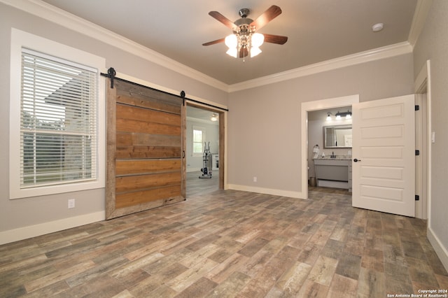 unfurnished bedroom featuring ornamental molding, ceiling fan, wood-type flooring, a barn door, and connected bathroom