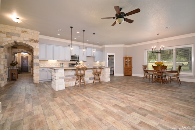 kitchen featuring pendant lighting, white cabinets, a center island with sink, light wood-type flooring, and a kitchen bar