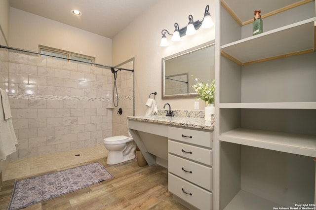 bathroom featuring hardwood / wood-style floors, vanity, toilet, and a tile shower