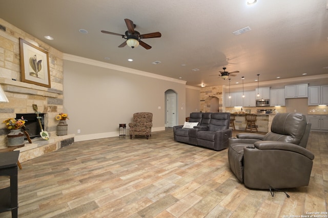 living room featuring a stone fireplace, ceiling fan, light hardwood / wood-style flooring, and ornamental molding