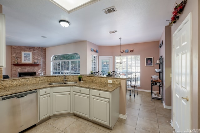 kitchen featuring light stone counters, stainless steel dishwasher, sink, an inviting chandelier, and a fireplace