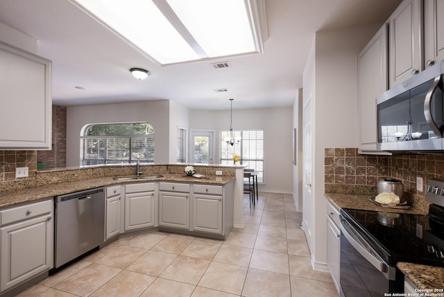 kitchen with stainless steel appliances, a sink, decorative backsplash, a peninsula, and plenty of natural light