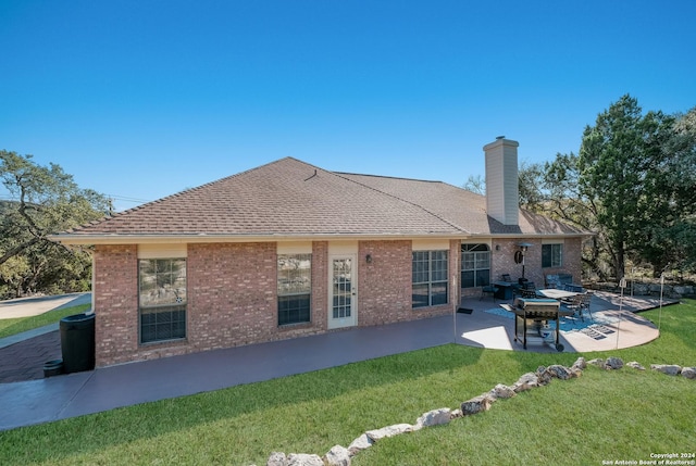 rear view of house featuring a patio, a lawn, a chimney, brick siding, and roof with shingles