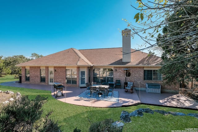 back of house featuring brick siding, a yard, a patio, and a chimney