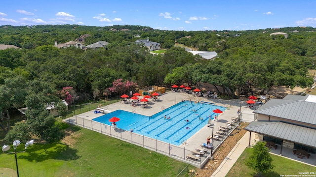 community pool featuring fence, a patio, and a forest view