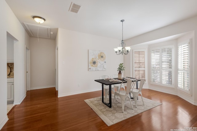 dining room featuring attic access, wood finished floors, baseboards, and a chandelier
