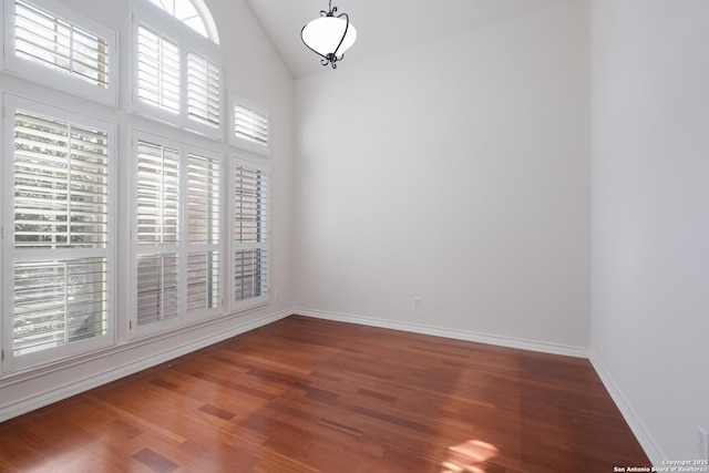 unfurnished dining area featuring wood finished floors, high vaulted ceiling, and baseboards