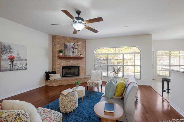 living area with wood finished floors, a brick fireplace, a ceiling fan, and baseboards
