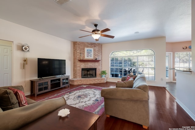 living room with a textured ceiling, ceiling fan, dark hardwood / wood-style flooring, and a fireplace